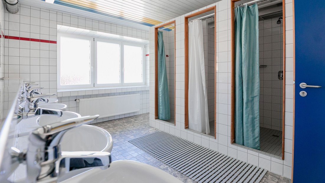 Banheiro de azulejo branco na casa de veraneio com várias pias e chuveiros