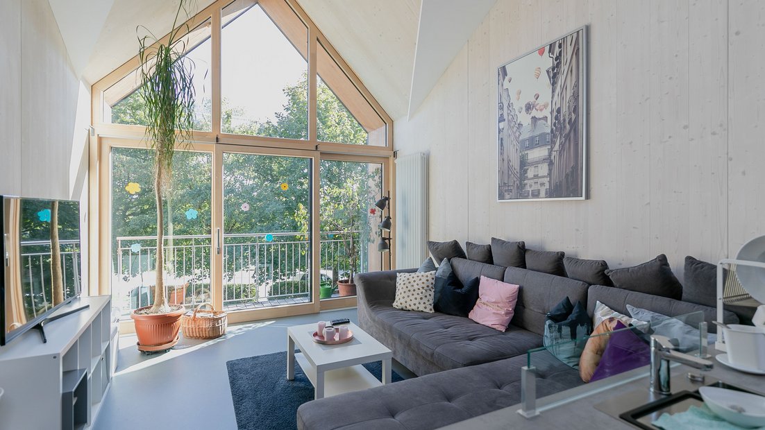 Área comum aconchegante lá em cima com grande canto de sofá cinza e vista através de uma grande janela de varanda
